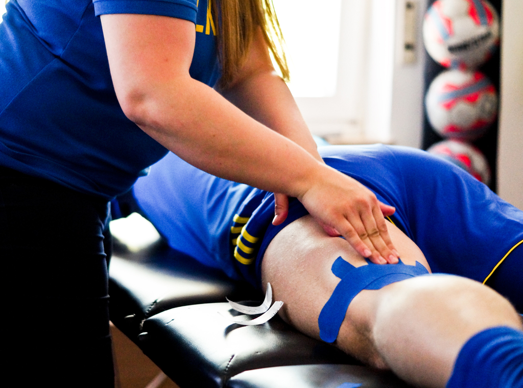 Fisioterapeuta aplicando tratamiento manual y vendaje neuromuscular en la pierna de un paciente durante una sesión de fisioterapia deportiva en el Centro Médico de Rehabilitación Majadahonda.